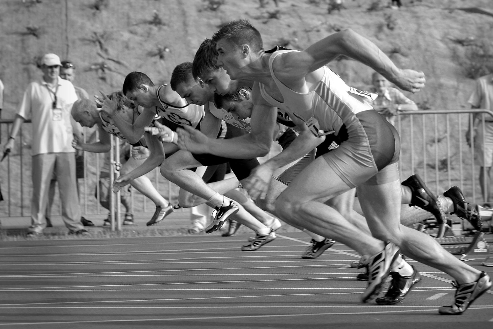 athletes running on track and field oval in grayscale photography